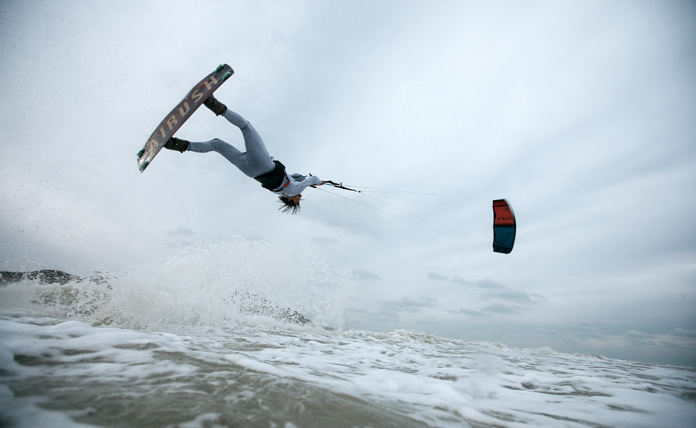 Un kitesurfeur à l'envers haut au-dessus de l'eau en plein saut, l'aile décalée sur le côté