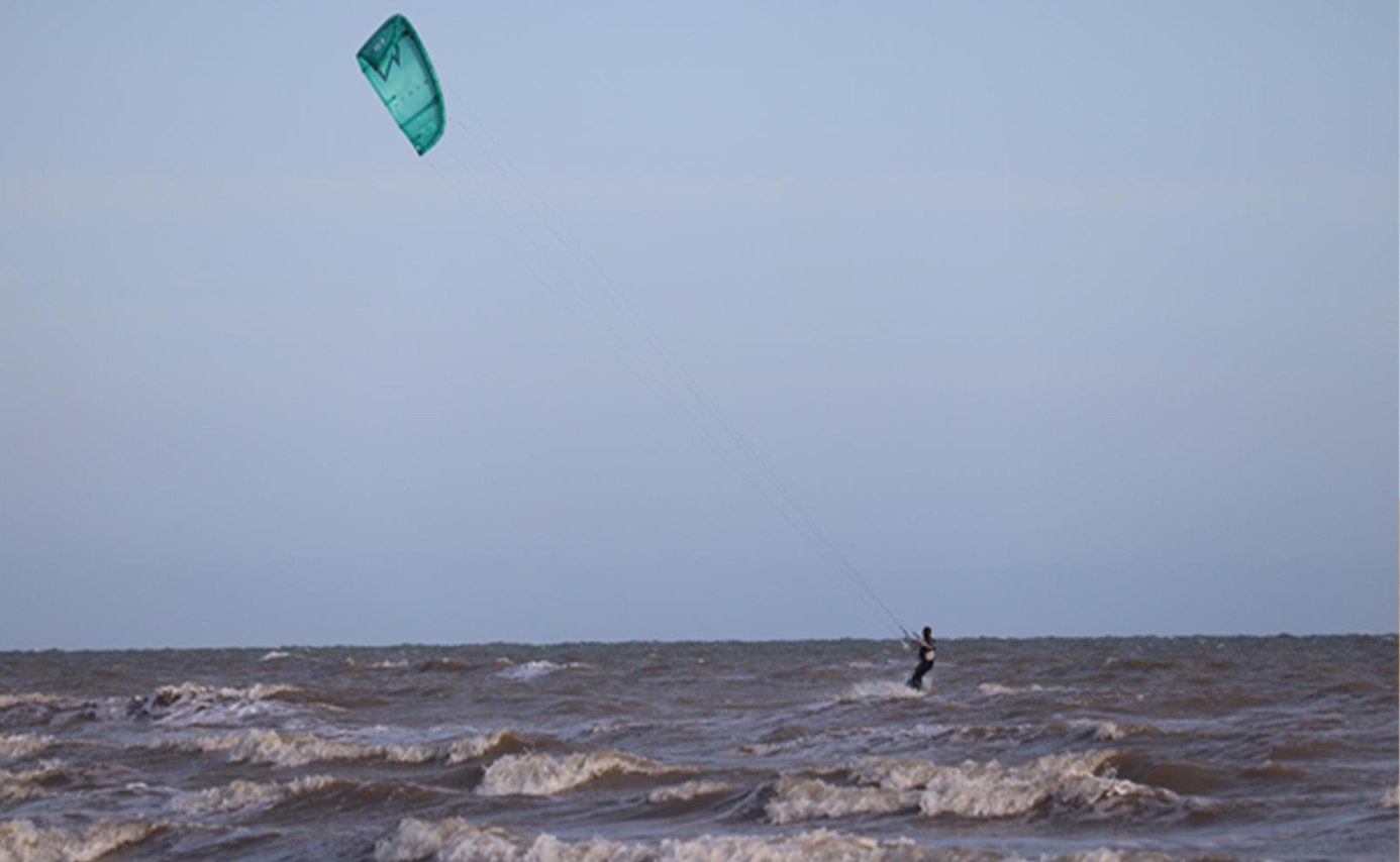 Kitesurfeur solitaire au large sur une mer grise agitée, petite aile turquoise haut dans le ciel